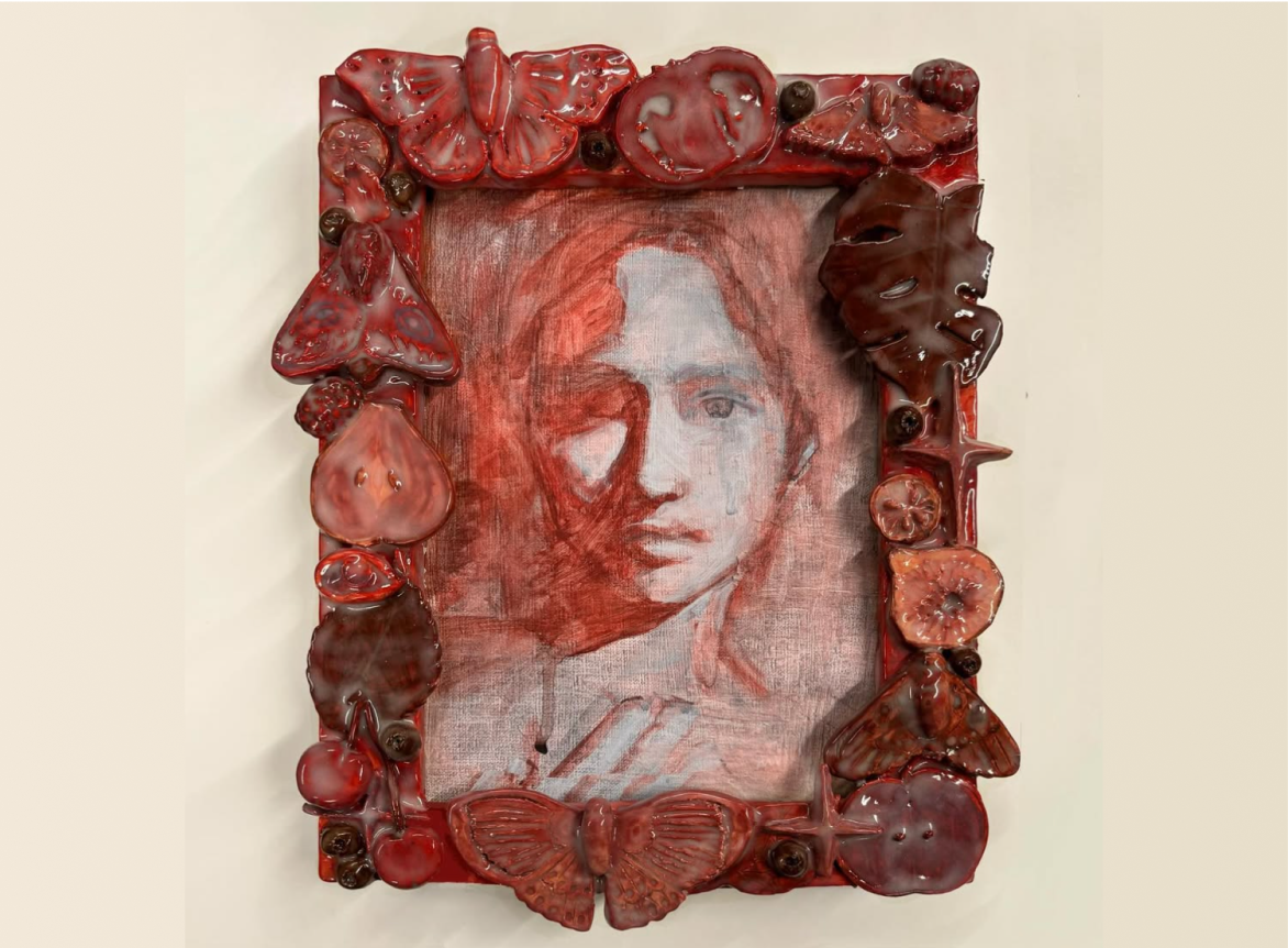 A red portrait painting surrounded by a sculpted ceramic frame of fruit and moths