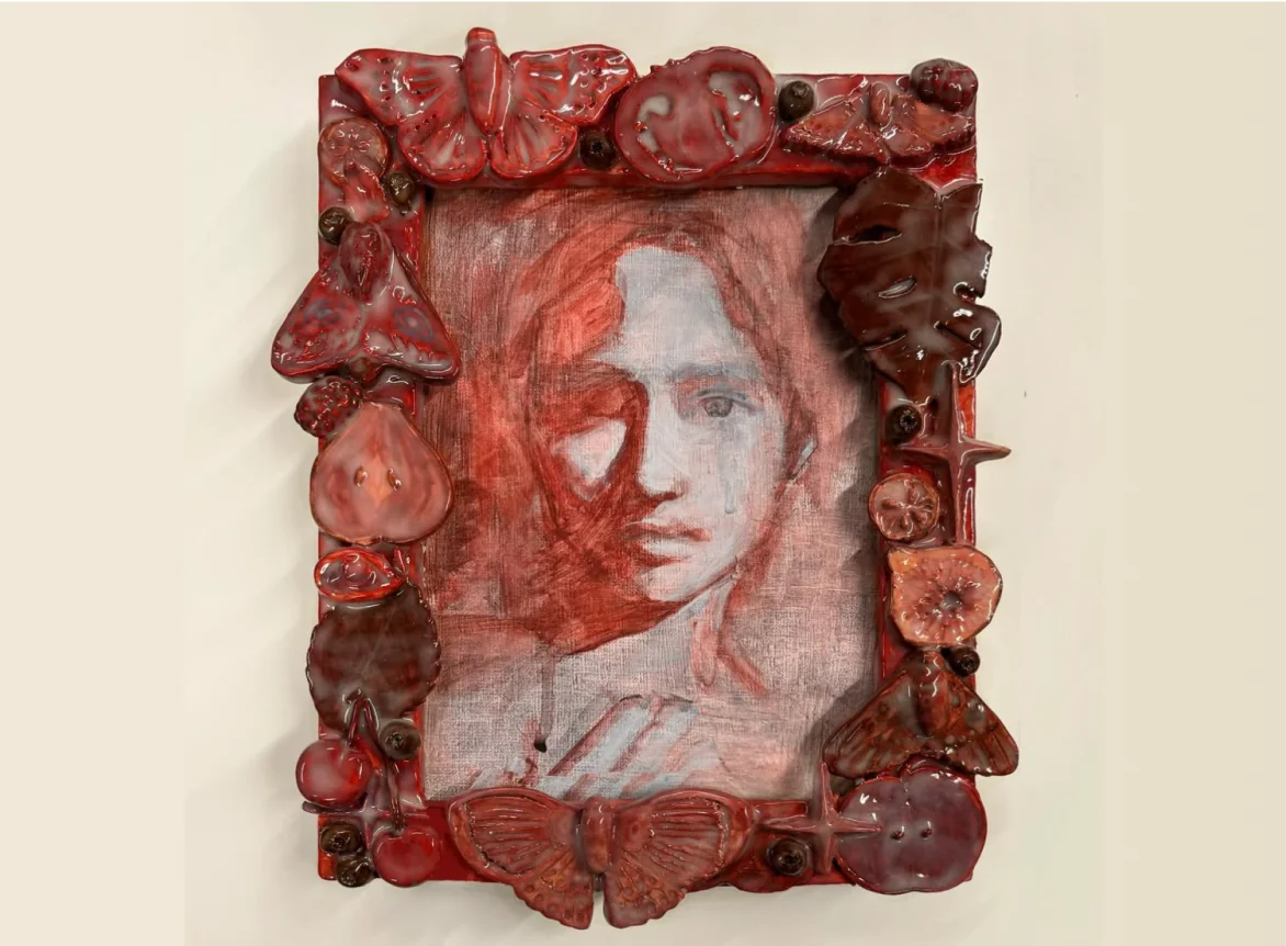 A red portrait painting surrounded by a sculpted ceramic frame of fruit and moths