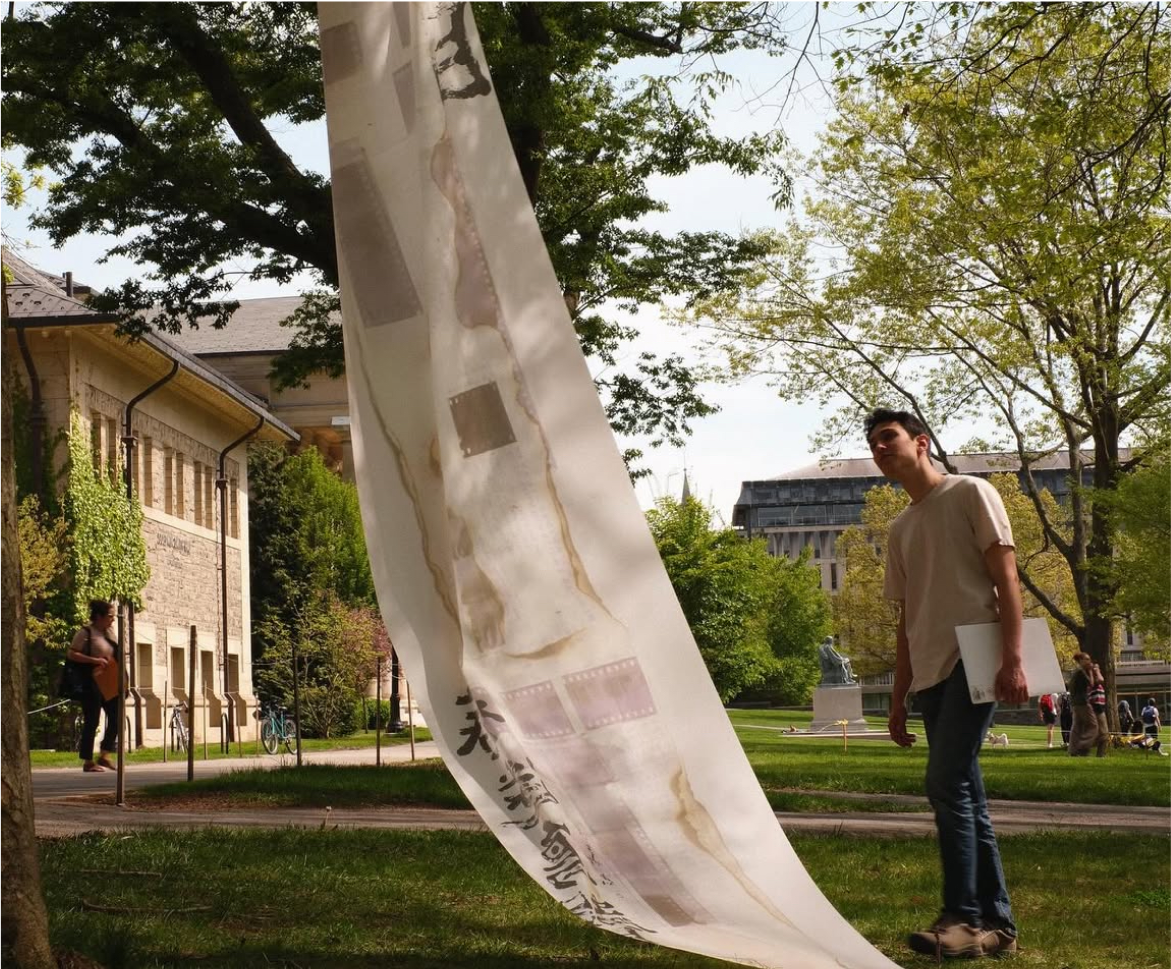 A person viewing a long translucent fabric installation suspended outdoors on a Cornell lawn