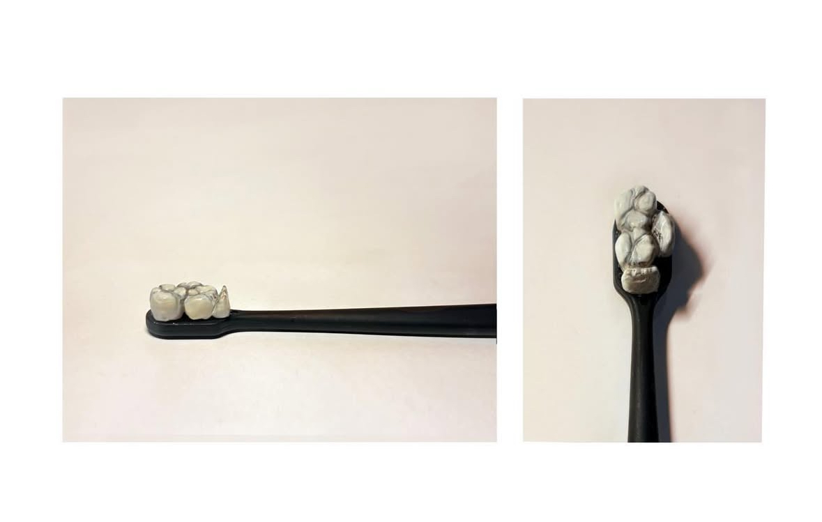 A black sculpted toothbrush with a tooth-shaped clay head on a cream background