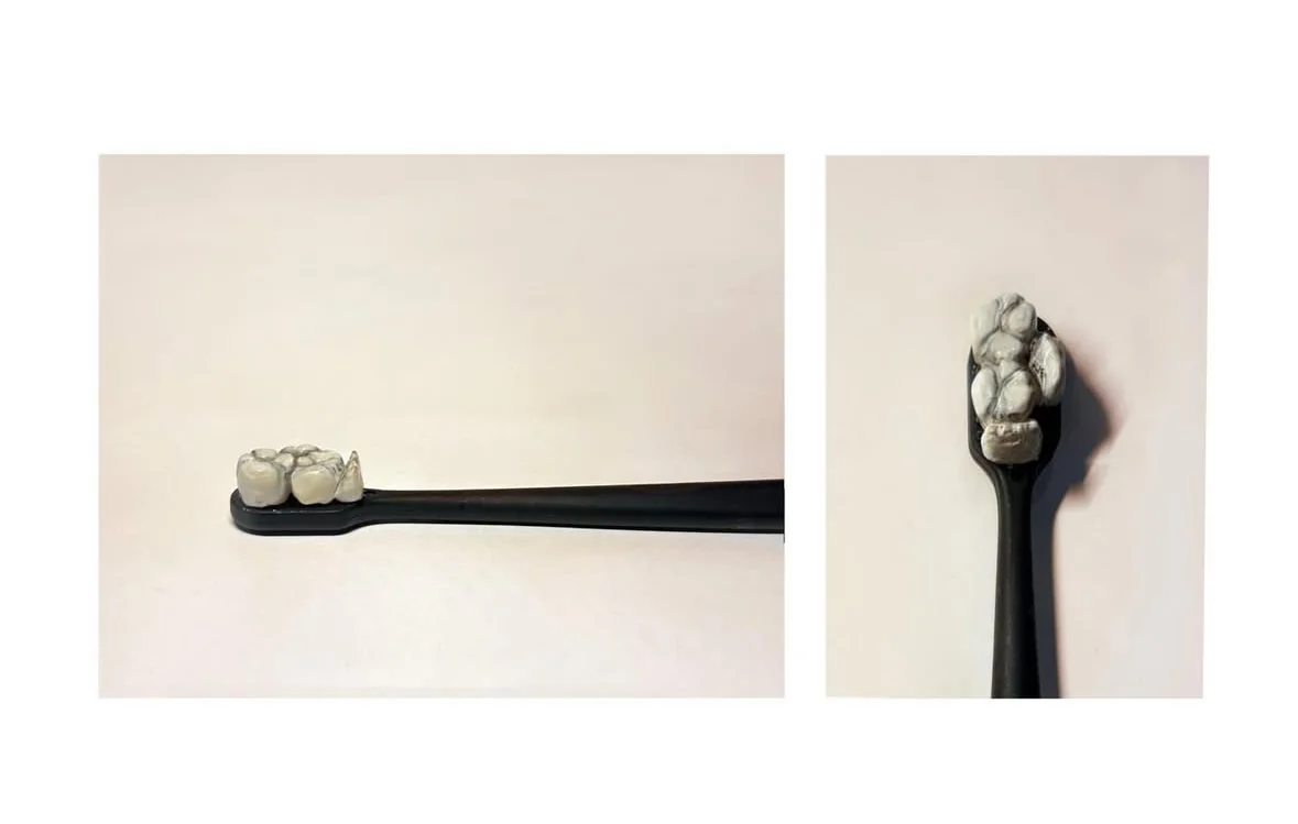 A black sculpted toothbrush with a tooth-shaped clay head on a cream background