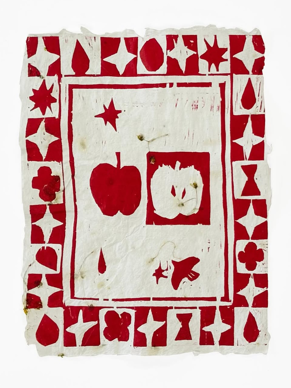 A red-and-white woodblock print of apples, flowers, and geometric symbols on handmade paper